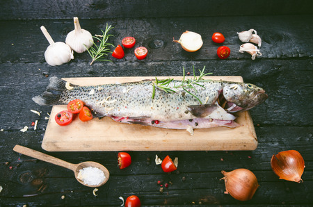Fresh fish on a vintage black, burnt table. Wooden table. Fish with vegetables, salt, oil, herbs. Concept of cooking. Healthy and dieting food. Detailの写真素材