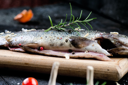 Fresh fish on a vintage black, burnt table. Wooden table. Fish with vegetables, salt, oil, herbs. Concept of cooking. Healthy and dieting food. Detailの写真素材