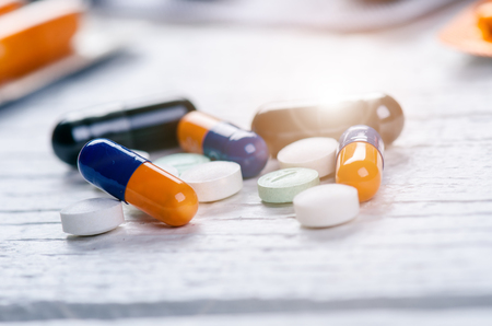 Pharmacy background on a white wooden table. Tablets on a white background. Pills. Medicine and healthy. Close up of capsules. Different kind of pills with lens flareの写真素材