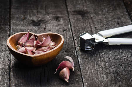 Cloves of garlic on a wooden black table. Fresh garlic bulb with iron garlic press. Vintage background. Farmer. Medicine and healthy. Traditional medicine.の写真素材