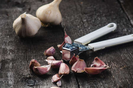 Cloves of garlic on a wooden black table. Fresh garlic bulb with iron garlic press. Vintage background. Farmer. Medicine and healthy. Traditional medicine.の写真素材