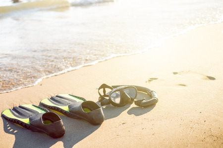 Swim flippers with snorkel, mask and feet steps on a sandy beach. Water sports. Snorkeling. Travel and holiday concept. Fins and scuba mask.の写真素材