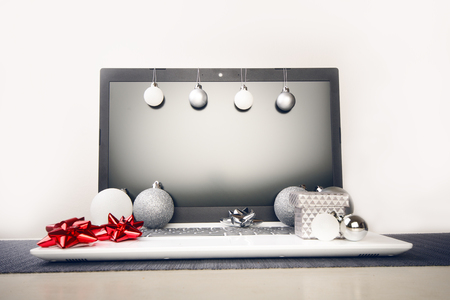 Christmas decoration on a computer. Red and silver ribbon on laptop desktop. Computer on a wooden table and white wall. Business concept during a holiday. Xmas concept.の写真素材