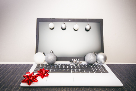 Christmas decoration on a computer. Red and silver ribbon on laptop desktop. Computer on a wooden table and white wall. Business concept during a holiday. Xmas concept.の写真素材