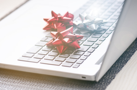 Christmas decoration on a computer. Red and silver ribbon on laptop desktop. Computer on a wooden table and white wall. Business concept during a holiday. Xmas concept.の写真素材