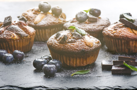 Fresh, blueberry muffins with strawberry, chocolate on a wooden board and stone background with sugar and fruits. Food background. Concept of pastry.の写真素材