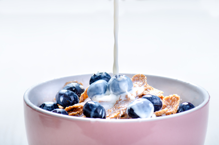 Full muesli bowl on a white table with blueberry. Healthy breakfast cereals with milk, seed, fruit. Oat flakesの写真素材
