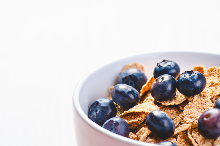 Full muesli bowl on a white table with blueberry. Healthy breakfast cereals with milk, seed, fruit. Oat flakesの写真素材