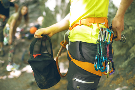Detail of young man who preparing on a climb and standing a next to rock wall. Equipment for...