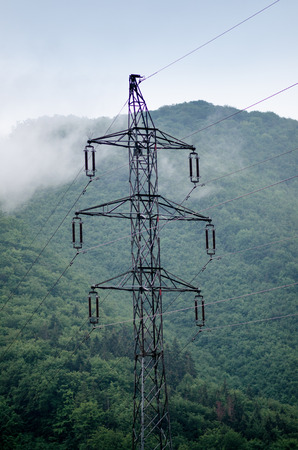 High voltage towers in a middle of forests and meadow. Electricity pylon with dark atmosphere in a nature. Rainy day. Power transmition towers.の写真素材