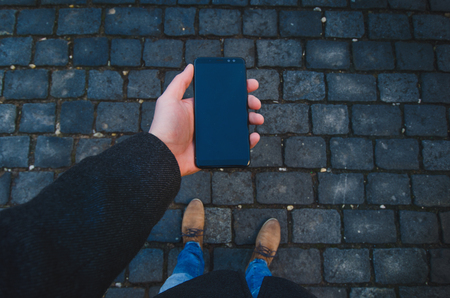 Male hand using smart phone on the street. Concept of technology and social network. Business man with watches, coat and take a photo.の写真素材