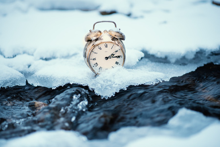 Frozen time. A clock on an ice next to the water. Extreme weather situation. Snow falling on a clock...