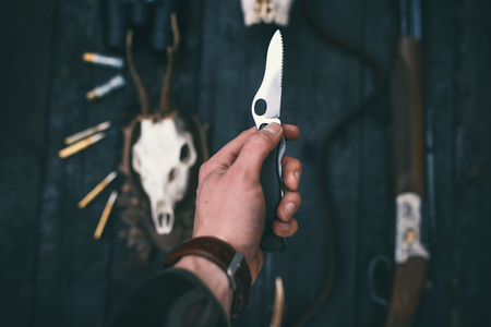 Professional hunter keep a knife in hand. Background consist of rifle, gun, ammunition, trophy of roe deer.の写真素材