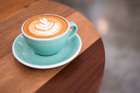 a cup of cappuccino with latte art on wooden background. Beautiful foam, greenery ceramic cups, stylish toning, place for text.の写真素材