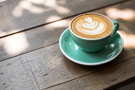 Close up coffee cup with leaf shape latte art on wood table backgroundの写真素材