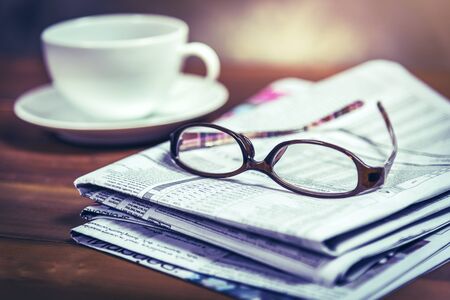 Glasses on pile of newspaper with coffee cup in background.Vintage tone photo with selective focus...