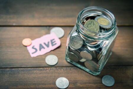 Coins in glass jar with the word save in background. Photo with vintage tone. Saving money concept.の写真素材