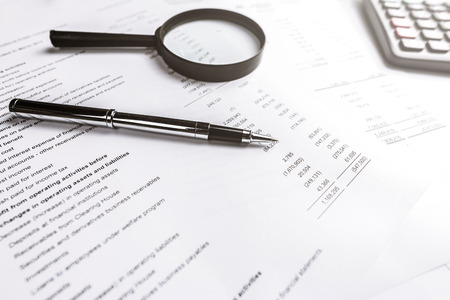 Pen and magnifying glass on finacial statement paper. Analysis business concept. Photo with sunlight filter effect.の写真素材