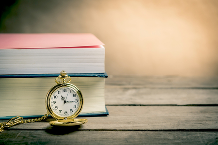 Books with vintage pocket watch on wooden table.の写真素材