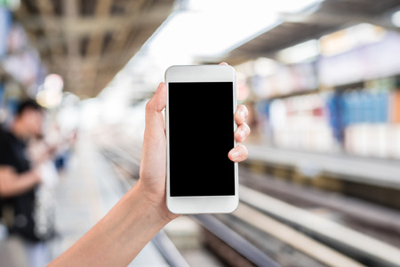 Hand holding mobile phone at railway platform stationの写真素材