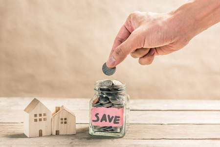 Male hand putting coin in glass jar of coin for saving money for buying houseの写真素材