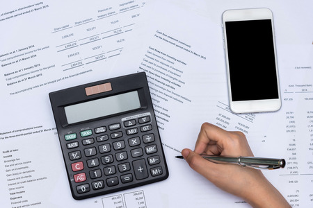 Top view of hand working with business financial data document with blank smart phone.