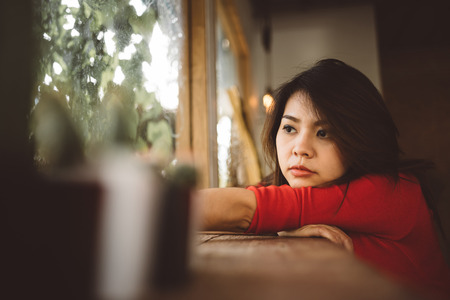 Portrait of lonely young Asian woman looking through a window.の写真素材