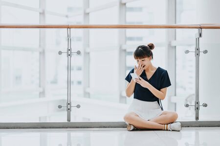 Young Asian girl surprised while sitting and using smart phone indoor.の写真素材