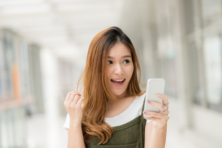 Young beautiful happy Asian girls laugh and smile while having fun with smartphone mobile indoor.の写真素材