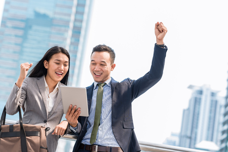 Young happy Asian businessman and woman celebrated success while looking in tablet outdoor.の写真素材