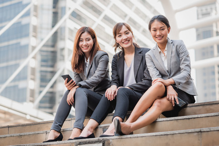 Three happy Asian Businesswoman colleague smile with confident while sitting on the stair outdoor.の写真素材