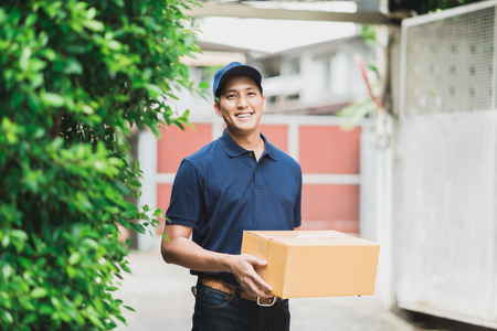 Happy Asian deliveryman holding cardboard box. Working with service mind.の写真素材