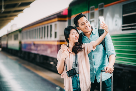 Happy Asian traveler couple taking selfie with smartphone at train station during vacation tripの写真素材