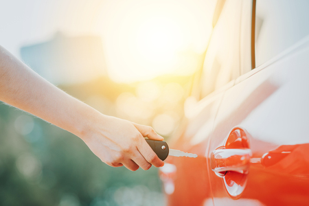 Woman hand holding car key unlocking a car door in sunlightの写真素材