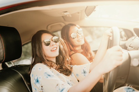 Young happy Asian girl best friends laughing and smiling in car during a road trip to vacation.の写真素材
