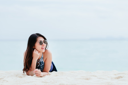 Portrait of happy young Asian woman lying at beach under a bright blue skyの写真素材