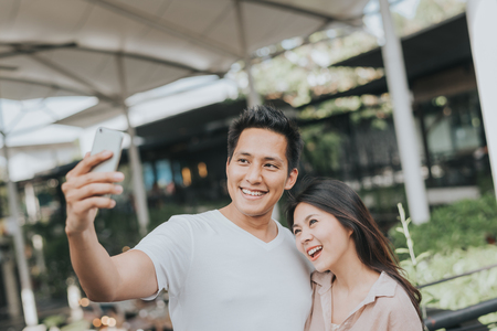 Happy smiling Asian having fun and taking selfies on smarthphone outdoorの写真素材