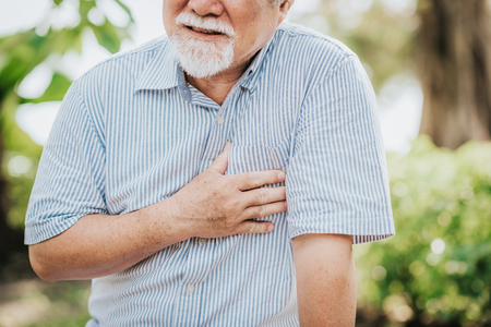 Cropped shot of senior man holding his chest and feeling pain suffering from heart attack outdoor at the parkの写真素材