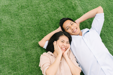 Happy and funny Asian couple in love relaxing on green grass at parkの写真素材