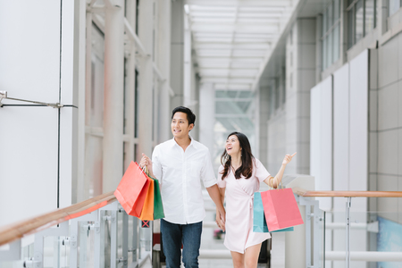Happy Asian couple holding colorful shopping bags and enjoying shopping, having fun together in mall. Consumerism, love, dating, lifestyle conceptの写真素材