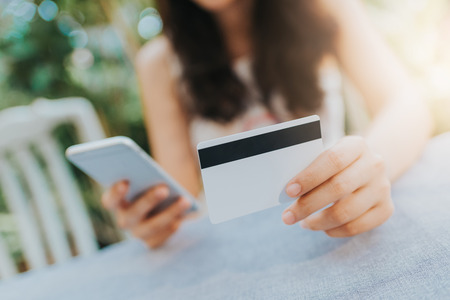 Close up shot of young woman holding credit card and using smartphone. Online shopping and payment conceptの写真素材