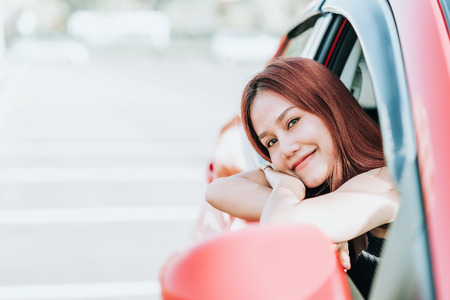 Shot of happy smiling young Asian woman leaning out her car windowの写真素材