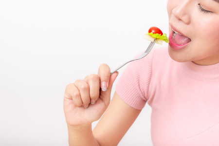 Close up shot of happy healthy woman eating salad vegetable from fork on white background