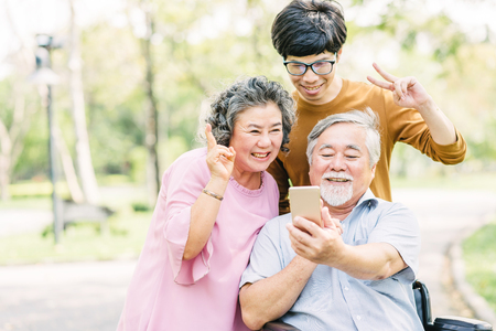 Happy Asian seniors family having fun with smartphone in the parkの写真素材