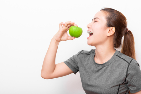 Asian woman with detal braces bites green apple on white backgroundの写真素材