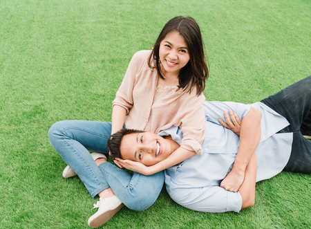 Happy Asian couple in love relaxing on green. Man lying on his girlfriend lap.の写真素材