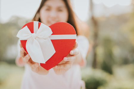 Woman presenting heart shape gift box outdoorの写真素材