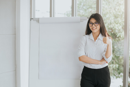 Happy confident Asian woman showing thumb up with blank flipchart for your content in meeting roomの写真素材