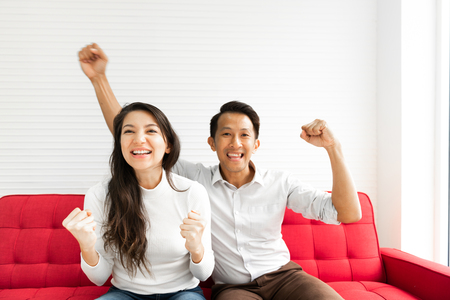 Couple celebrating and cheering success on the couchの写真素材