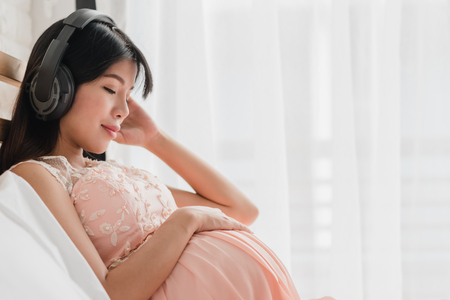 Asian pregnant woman relax listening music from headphones on bedの写真素材
